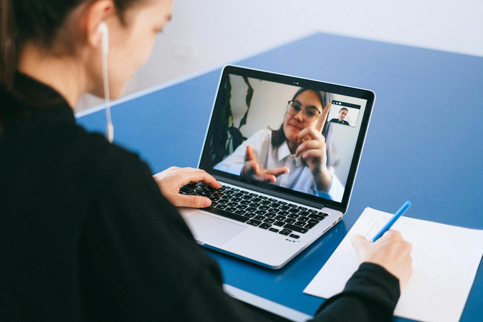 Woman participating in a virtual meeting, taking notes during a video conference on a laptop.